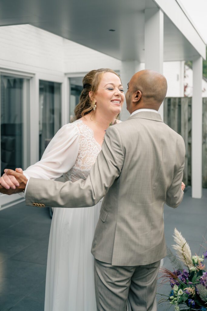 a bride and groom stand smiling at each other with their hands clasped and their arms wide spread