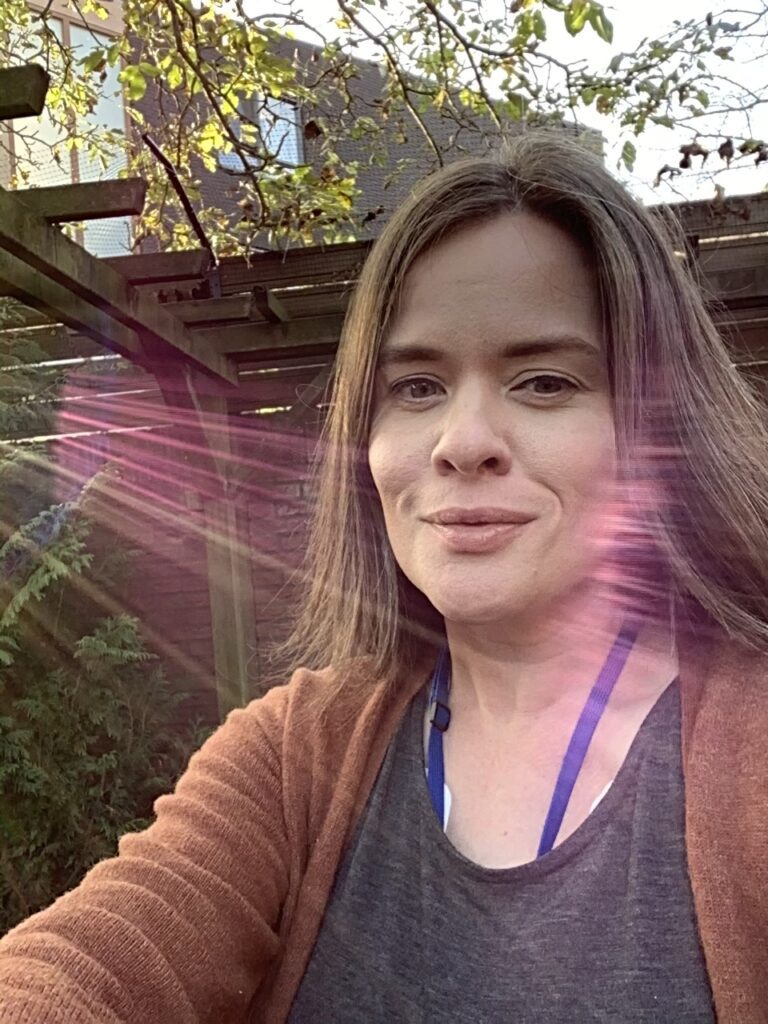 A woman stands looking at the camera with a heart monitor just visible around her neck