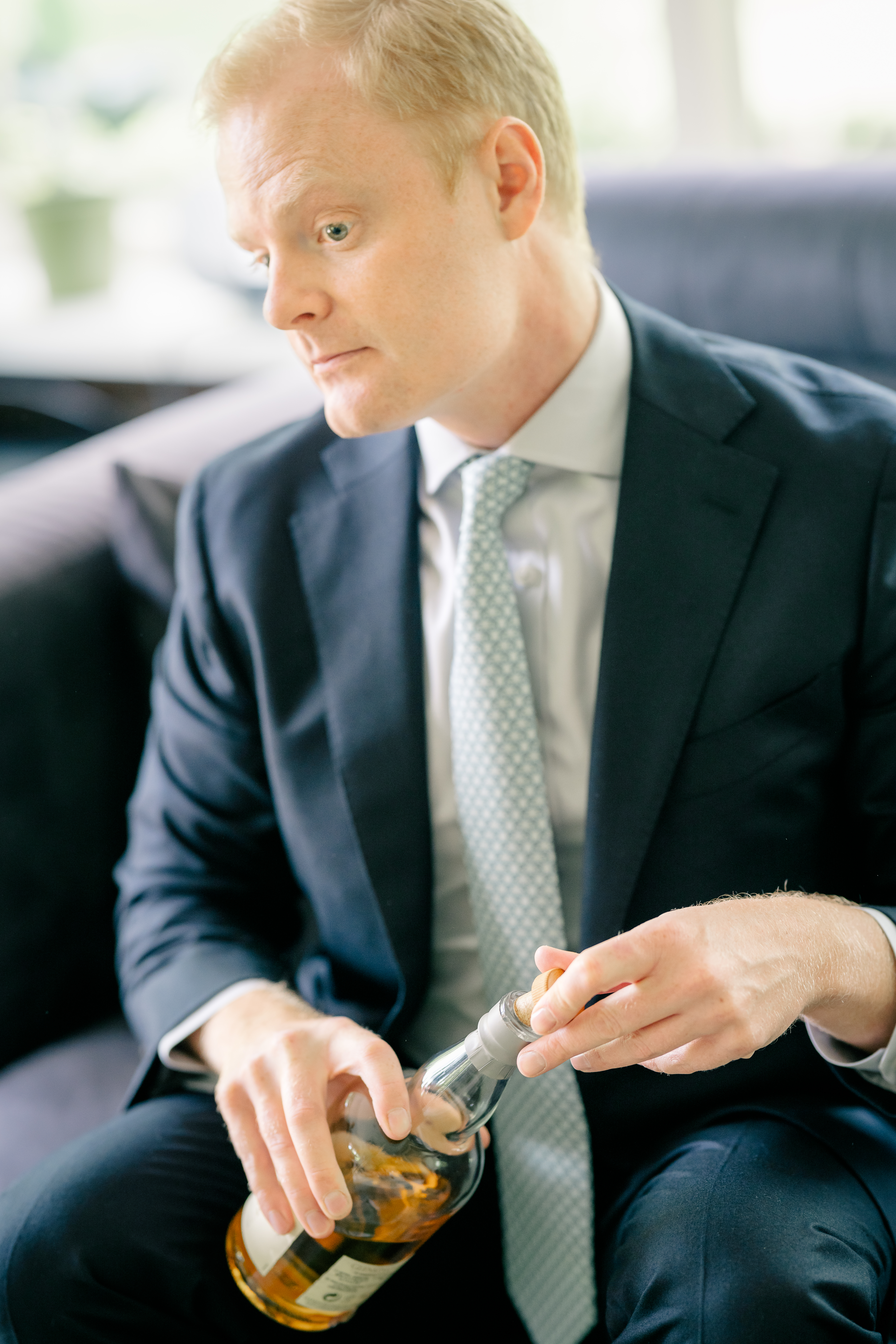 The groom sits and prepares to open a bottle while getting ready for the wedding