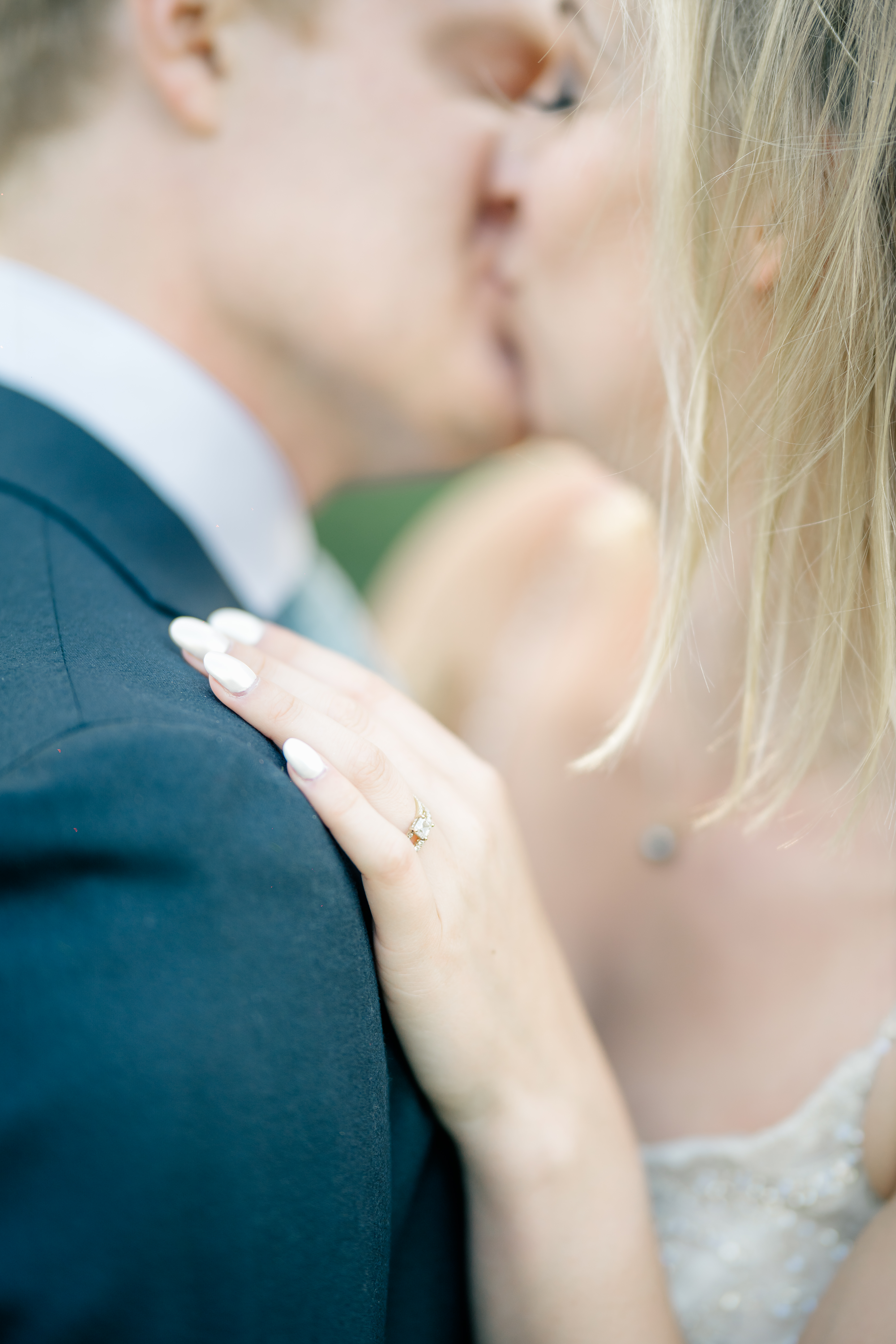 detail shot of ring on bride's hand whilst bride and groom kiss