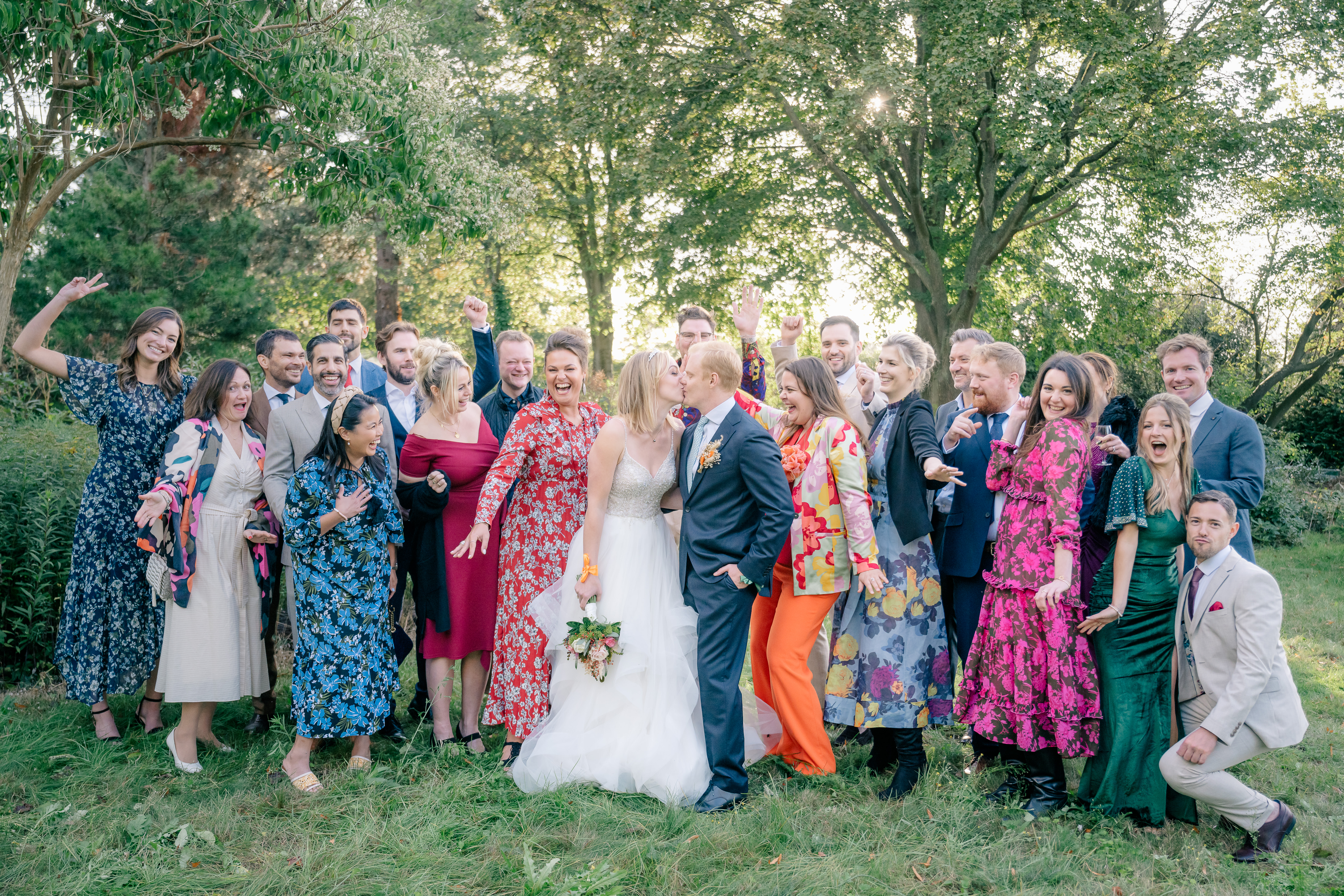 A bride and groom kiss whilst their friends cheer them on in a late afternoon september garden wedding