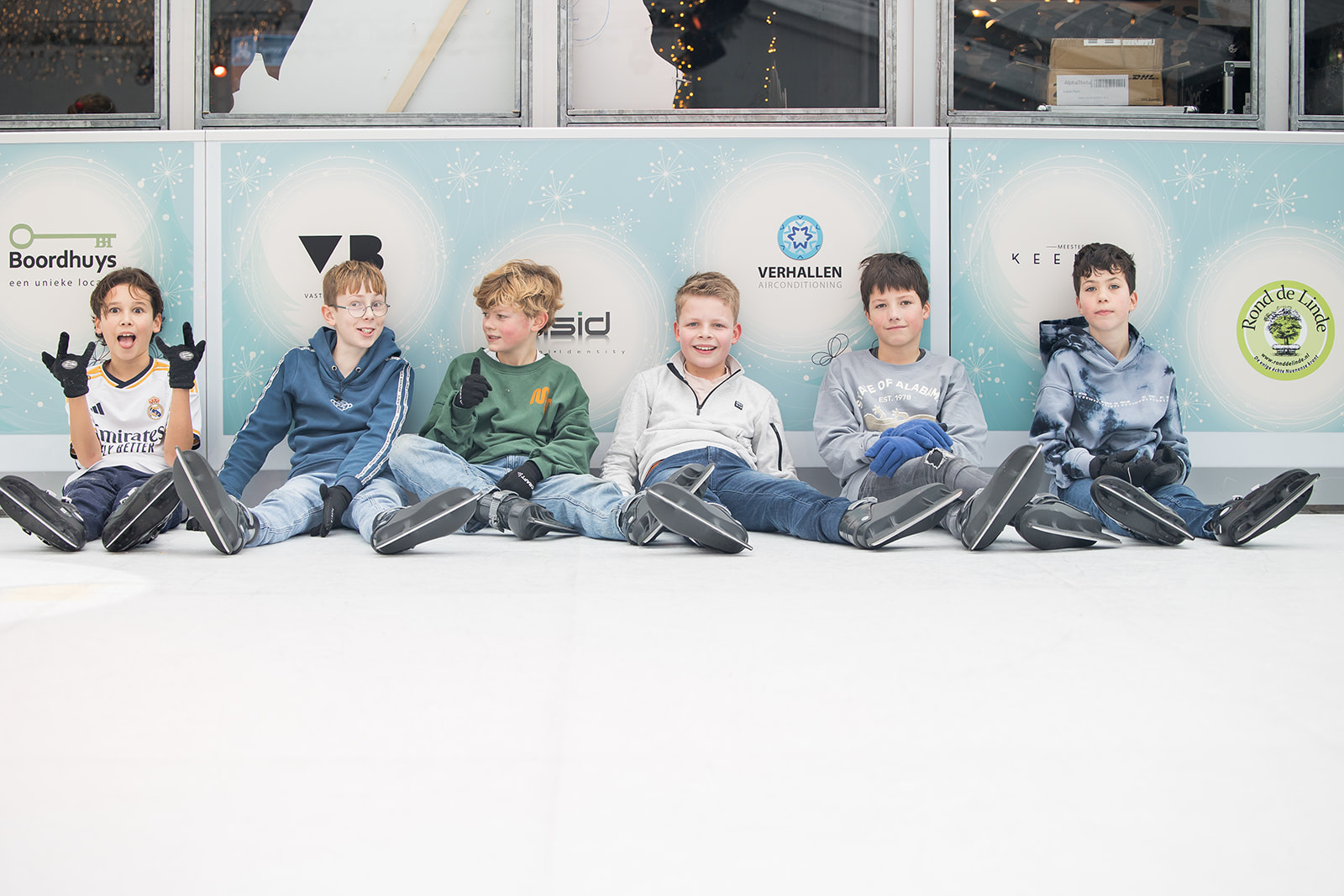 Groep kinderen zit met schaatsen op het ijs tijdens schoolschaatsen bij Dwers op het ijs in Nuenen.